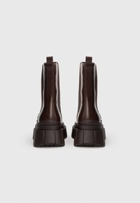 Hnědé kotníkové boty s lesklým povrchem, elastickými bočními panely, robustní platformovou podrážkou a poutky pro snadné obouvání. Texturovaný svršek a pevná konstrukce.