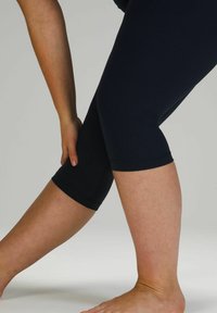 Leggings de sport noirs, à mi-cuisses, au design ajusté. Texture lisse avec une taille élastique et des coutures plates. Un pied nu positionné à proximité.