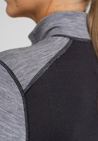 Grå atletisk top med høj krave, tekstureret stof og sorte mesh-paneler til ventilation. Udviklet med kontraststing.