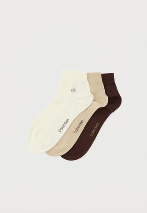 Three pairs of socks in cream, beige, and dark brown. Each features a smooth texture and "CK" logo printed near the cuff.