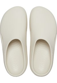 Helle beige Clogs mit offenem Rücken, aus glattem Kunststoff gefertigt. Die strukturierten Einlagen verfügen über kleine erhabene Punkte. Das Logo "Crocs" ist auf den Seiten geprägt.