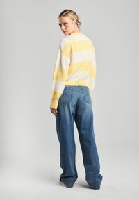 Neulepaita, jossa on keltaisia ja valkoisia raitoja, pyöreä kaula-aukko ja ribbaushelma; yhdistettynä löysiin, vaalennettuihin sinisiin farkkuihin.