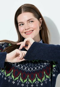 Maglione blu navy lavorato a maglia con design Fair Isle; presenta motivi rossi, verdi e bianchi; polsini a coste; modello che forma un cuore con le mani.