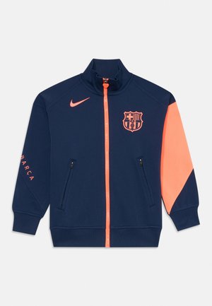 Veste zippée marine avec col montant, accents corail, poches intégrées et logo du FC Barcelone sur la poitrine. Fabriquée en tissu léger et lisse.