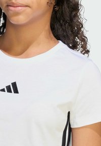 Biela bavlnená tričko s čiernym logom Adidas na hrudi, okrúhlym výstrihom a čiernym akcentom na rukáve.