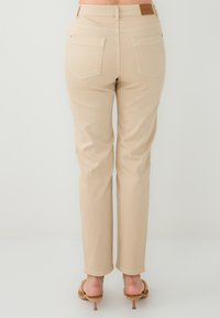 Pantalons en coton beige avec une coupe droite, poches arrière et texture lisse. Présente une étiquette en cuir au niveau de la taille.