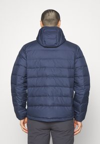Giacca puffer blu navy con cappuccio, caratterizzata da sezioni orizzontali trapuntate e una texture liscia e lucida. Polsini regolabili e design elegante.