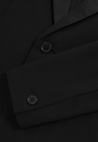 Manga y panel frontal de blazer formal negro mostrando dos botones negros y detalle de solapa en tela lisa.