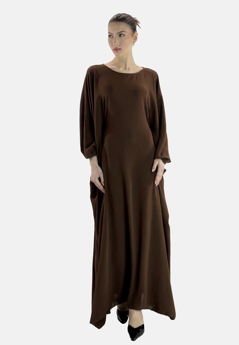 Robe maxi marron à manches longues avec une coupe décontractée et un col rond. Fabriquée en tissu doux et fluide. Portée avec des talons noirs à bout pointu.