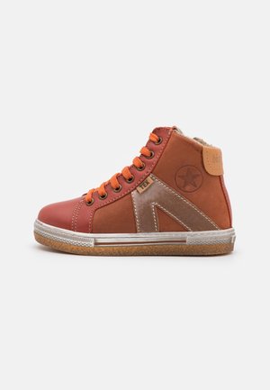Basket montante marron et orange avec des lacets orange, une semelle en caoutchouc, un emblème étoile et une étiquette en tissu sur le côté, sur fond uni.