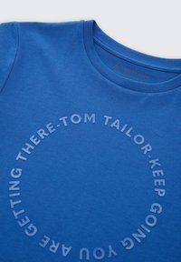 Camiseta de algodón azul con un diseño de texto circular que dice "TOM TAILOR KEEP GOING THERE - YOU ARE GETTING." Textura suave y escote redondo.