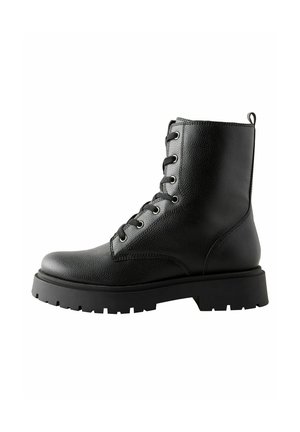 Botas de tobillo negras con cordones, de cuero texturizado, puntera redonda y suela de goma gruesa. Presentan ojetes plateados y una lengüeta en la parte posterior.