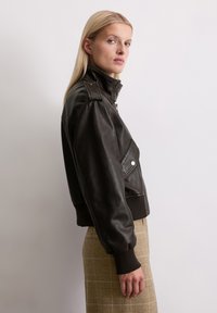 Braune Lederjacke mit hohem Kragen, gerippten Bündchen und einem asymmetrischen Reißverschluss. Verfügt über Schulterklappen und eine strukturierte Oberfläche.