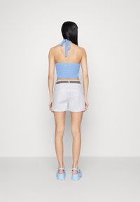 Haut halter en crochet bleu clair avec un col noué, assorti à un short blanc et des chaussures à plateforme bleues. Texture lisse et design décontracté.