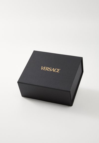 Melns taisnstūra kaste ar teksturētu virsmu un zelta "VERSACE" logo augšpusē. Aprīkota ar eņģēm, kas ļauj to atvērt un aizvērt.