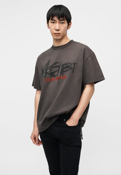 Γκρι υπερμεγέθη T-shirt με μαύρο και κόκκινο γραφικό σχέδιο με την επιγραφή «NEW YORK». Συνδυασμένο με μαύρα τζιν, παρουσιάζοντας ένα casual, άνετο στύλ.