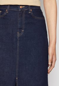 Mörk jeanskjol med synliga orangea sömmar, utrustad med en frontslits, femficksdesign och knäppning i midjan.