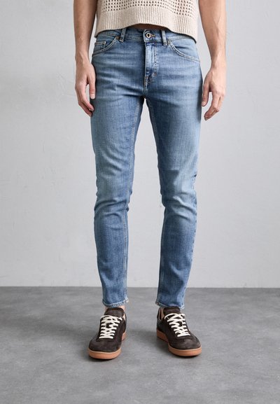 Svetle modré slim-fit džíny s opraným vzhledem, pětikapsový design a zapínání na knoflík, zkombinované s tmavě hnědými teniskami.