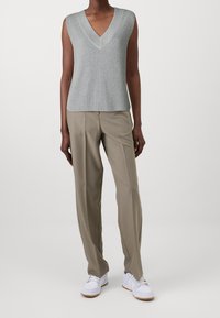 Lichtgrijze mouwloze V-hals gebreide top gecombineerd met beige op maat gemaakte broeken en witte sneakers. De top heeft een geribbelde textuur.