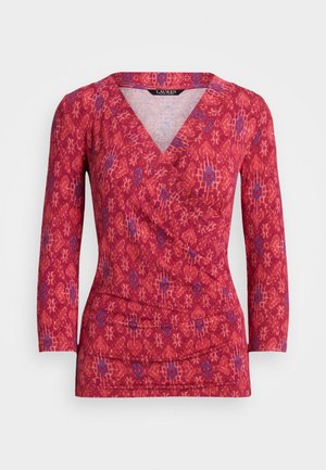 Czerwona bluzka kopertowa z długim rękawem, z geometrycznym kwiatowym wzorem w odcieniach różu i fioletu oraz dekoltem w kształcie litery V.
