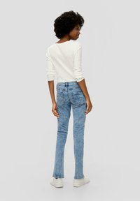 Witte lange mouwen top en lichtblauwe denim jeans met een slim fit, achterzakken en subtiele stiksels. Schoenen zijn witte sneakers.