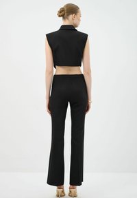 Black cropped vest with a collar paired with high-waisted black trousers. Smooth fabric, fitted design, and flared hem, featuring a minimalistic style.