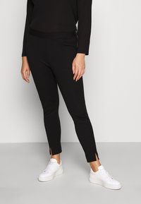 Leggings noirs avec un design ajusté, d�étail de zip sur le côté et petites fentes aux chevilles. Portés avec des baskets blanches pour le contraste.