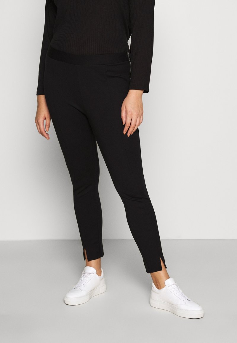 Leggings noirs avec un design ajusté, détail de zip sur le côté et petites fentes aux chevilles. Portés avec des baskets blanches pour le contraste.