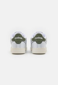 Bílé kožené tenisky s zelenými semišovými detaily, s nízkým střihem a texturovanou gumovou podrážkou. Na patě viditelné logo "Reebok".