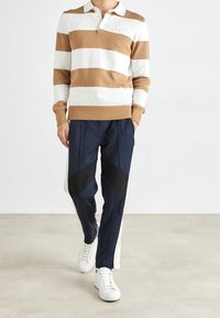 Randig stickad polo i vitt och karamell, med krage och ribbade ärmslut, kombinerad med marinblå byxor med svarta accenter och vita sneakers.