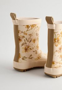 Bottes de pluie à motif floral en crème avec des accents beiges, en matériau en caoutchouc, semelles à grip texturé et tirettes en haut pour un enfilage facile.