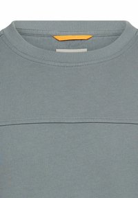 Lichtblauwe crewneck-trui met geribbelde textuur, voorzien van een contrasterend oranje accent op de achterkant van het juk. Minimalistisch ontwerp, zonder patronen.