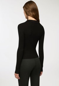 Czarna prążkowana bluzka z długim rękawem, dopasowanym krojem i kołnierzykiem, zestawiona z ciemnozielonymi spodniami w prążki o wysokim stanie.