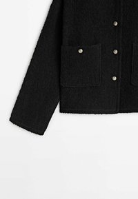 Svart fleecejacka med mjuk textur, långa ärmar, två framfickor och metallknappar. Enkel, rak design.