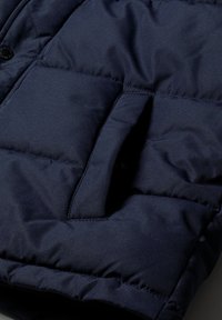 Détail d'une doudoune bleu marine avec des coutures visibles, une poche latérale et un tissu lisse et texturé.
