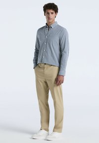 Blauw-wit geruit overhemd met knopen, beige broek en witte sneakers. Heeft lange mouwen en een ontspannen pasvorm.