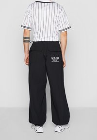 Vit randig tröja med svarta detaljer, ihop med svarta vida cargobyxor med patchfickor och logotryck på ryggen.