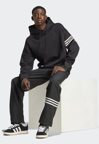 Sudadera negra con rayas blancas en las mangas, combinada con pantalones negros que tienen acentos a rayas y zapatillas de deporte en blanco y negro.