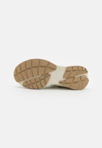 Suela de una zapatilla con una superficie de goma texturizada; colores beige claro y crema; presenta un patrón de banda de rodadura para agarre y estabilidad.