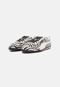 Ténis com padrão de zebra em esquema de cores branco e preto, apresentando um upper texturizado, atacadores pretos e uma sola de borracha.