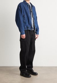 Denim Bomberjacke mit Reißverschluss vorne, elastischem Bund und zwei Seitentaschen. Kombiniert mit lockeren schwarzen Cargo-Hosen und schwarzen Schuhen.