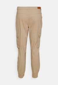 Pantalons cargo beiges avec des poignets élastiques, des poches latérales et une étiquette en simili cuir au niveau de la taille. Fabriqués en tissu doux et léger.