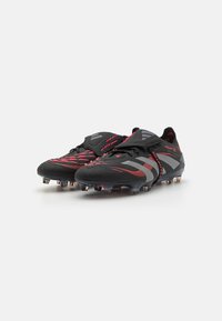 Zwarte voetbal schoenen met rode en grijze accenten, een gestructureerde bovenkant, vetersluiting en noppen op de buitenzool voor grip op het veld.