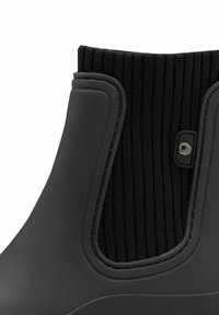 Botte de cheville en caoutchouc noir avec un dessus en tissu côtelé, des bords lisses et un petit logo en accent. Semelle texturée pour une meilleure adhérence.