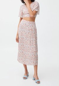 Ensemble crop top floral et jupe midi en tissu léger et doux. Présente un motif de fleurs multicolores sur fond blanc. Associé à des sandales à talons blocs bleues.