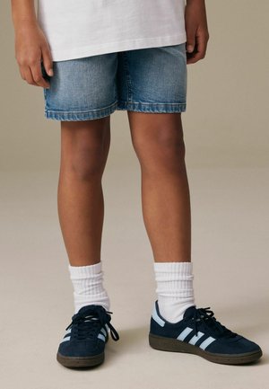 Hellblaue Jeansshorts mit klassischer Passform, kombiniert mit marineblauen Sneakern mit weißen Streifen und weißen, gerippten Socken.