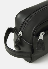 Borsa nera in pelle con finitura testurizzata, caratterizzata da cerniere argentate, un piccolo manico per il trasporto e una forma rettangolare compatta.