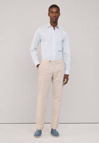 Camicia azzurro chiaro con strisce bianche, con bottoni e maniche lunghe, abbinata a chinos beige e scarpe slip-on blu. Design e fit puliti.