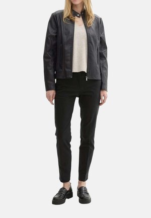 Veste en cuir noir au design ajusté, avec des coutures texturées et un col à pression. Associée à un pantalon noir et des chaussures noires à enfiler.