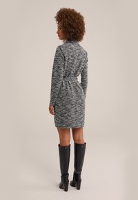 Abito in maglia con texture bianco e nero, aderente con una cintura in vita e maniche lunghe. Indossato con stivali neri a tacco alto fino al ginocchio.